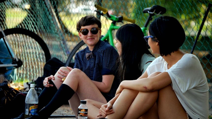 Three girls sit along the courtside watching a game of bike polo