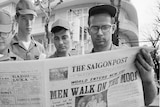 Four men in uniform pore over a newspaper covering the Apollo 11 mission