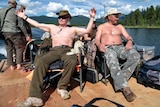 Vladimir Putin and Sergei Shoigu wear hats but no shirts as they lounge on a lakeside dock.