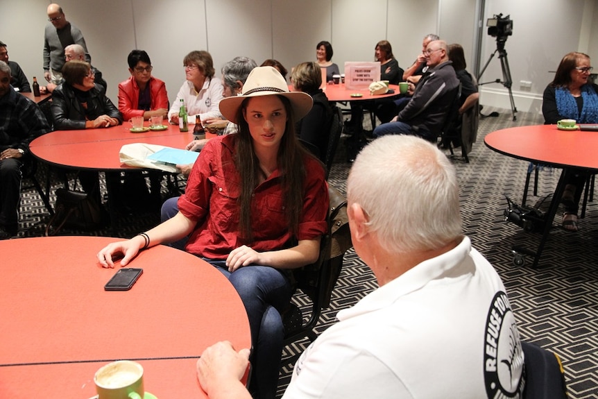 a young female wearing a cowboy hat and a serious expression sits facing an older man.