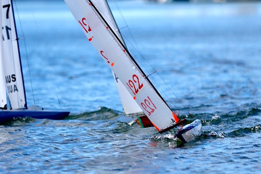 A close up of a model yacht in the water leaning.