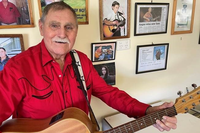 Man smiles in red country shirt and holds a guitar