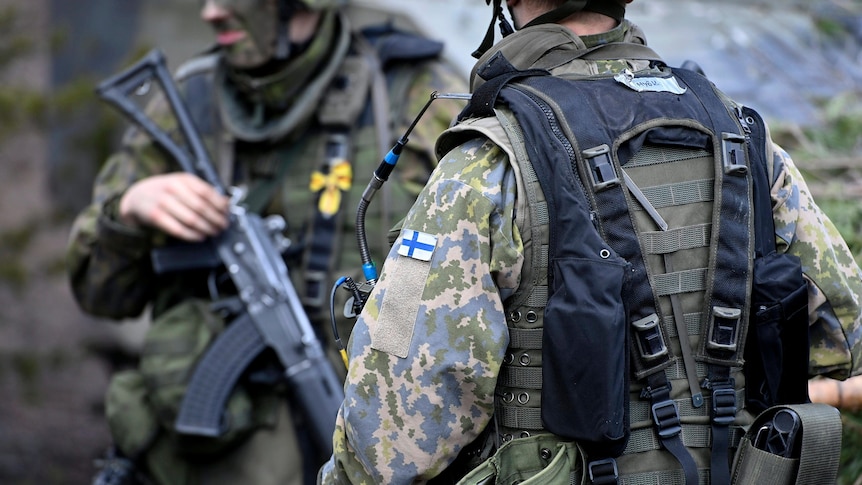 Soldiers in camouflage with a Finnish flag patch on their shoulders.