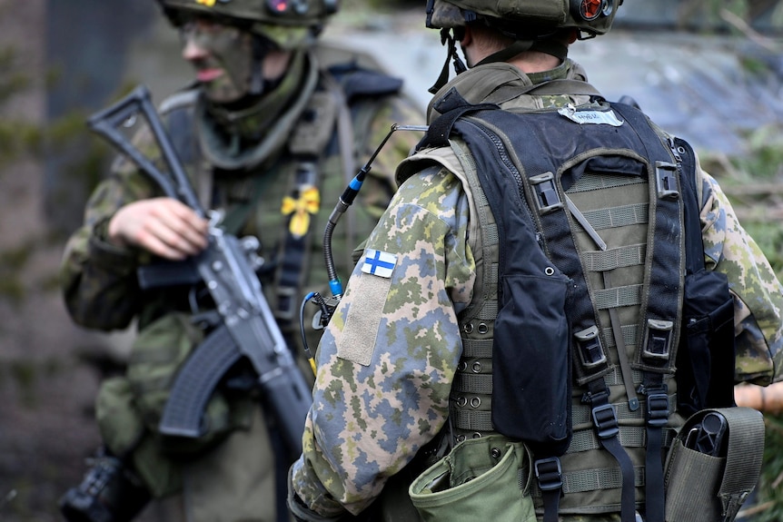 Soldiers in camouflage with a Finnish flag patch on their shoulders.