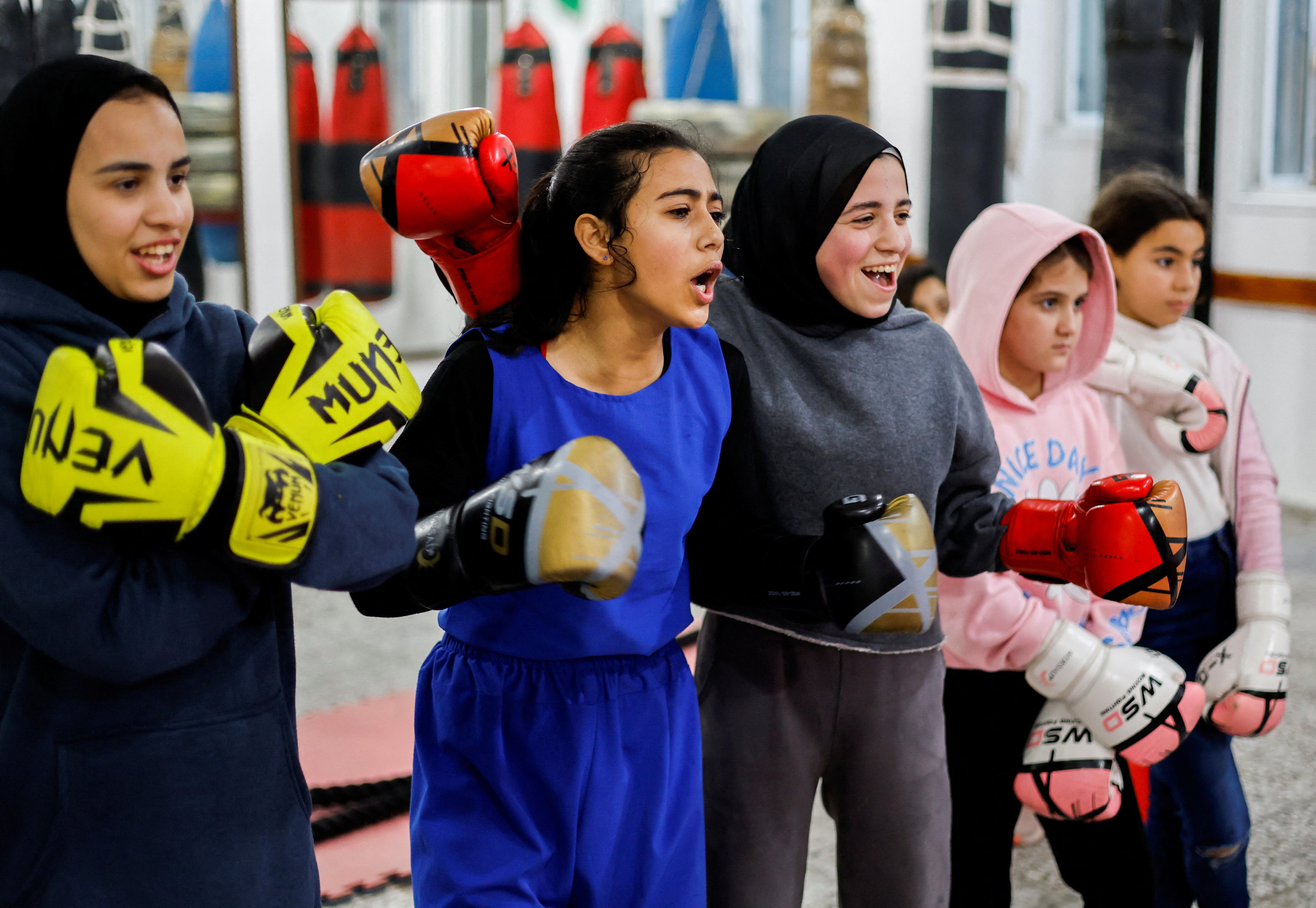 Five girls wearing boxing gloves stand next to eachother. 