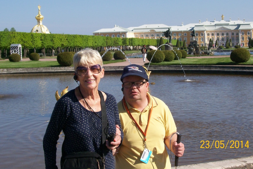 A msan and a woman in front of a lake and palace.