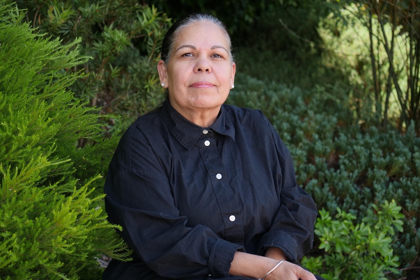 Nikki Foy sitting infront of green shrubs in a black shirt