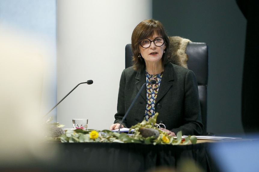 Victorian health minister seated at a justice commission hearing in front of a microphone
