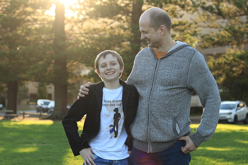 Val Kovalevsky holds his arm around his son Ivan at sunset with trees and golden light behind.
