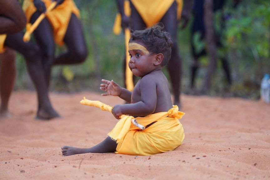 A baby sitting in the Garma 2019 opening ceremony in traditional costume.