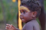 A baby sitting in the Garma 2019 opening ceremony in traditional costume.
