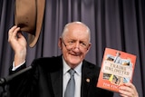 Tim Fischer smiles as he holds up his Akubra hat and a copy of his book, Trains Unlimited.