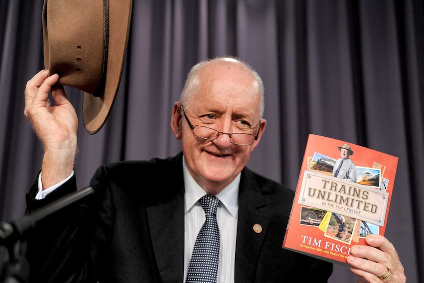 Tim Fischer smiles as he holds up his Akubra hat and a copy of his book, Trains Unlimited.