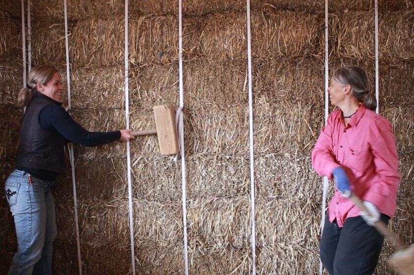 Two women use large wooden mallets to shift bales into place.