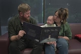Iris Leeson sits with her baby on her lap, sitting next to husband, reading book to baby