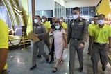 Police and court security personnel surround a small, pregnant woman wearing a light pink dress and thongs.