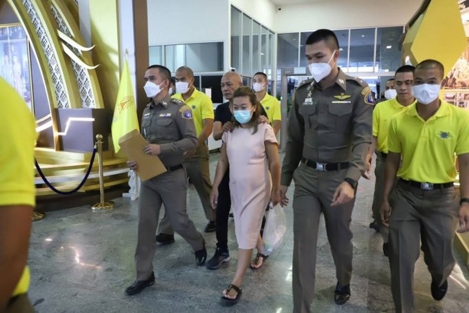 Police and court security personnel surround a small, pregnant woman wearing a light pink dress and thongs.