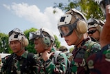 Three Indonesian soldiers at the front of a group, wearing camouflage uniforms, helmets and goggles 