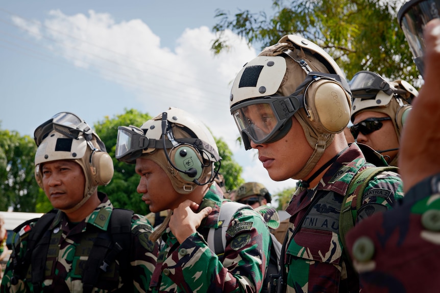 Three Indonesian soldiers at the front of a group, wearing camouflage uniforms, helmets and goggles 