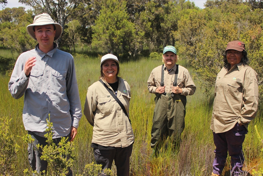 The four stand in a swamp wearing waders