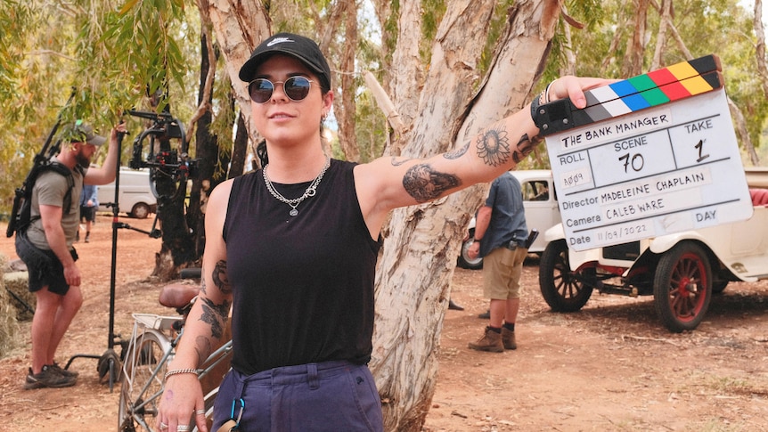 A woman wearing a black singlet holds up a clapperboard 
