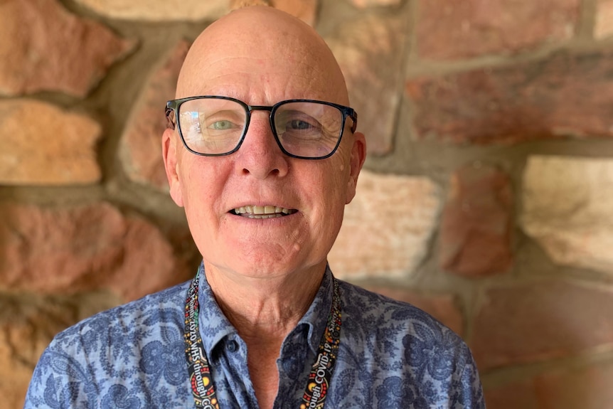 Bald man wearing black rimmed glasses and light blue shirt with dark blue paisley pattern.