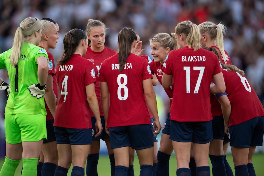 A Norwegian women's footballer looks at her gathered teammates and talks to them during a game.