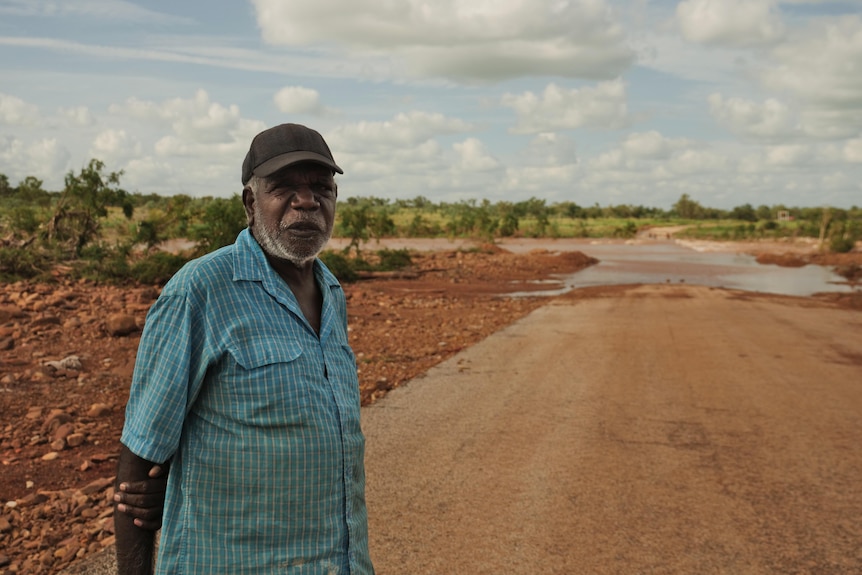 A man in a blue shirt stands by a flooded road. 