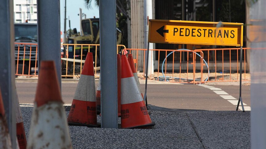 A photo of a sign redirecting pedestrians amid construction in a busy street.