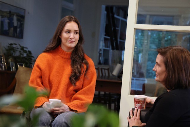 Woman wearing an orange jumper holding a tea cup with her mother.