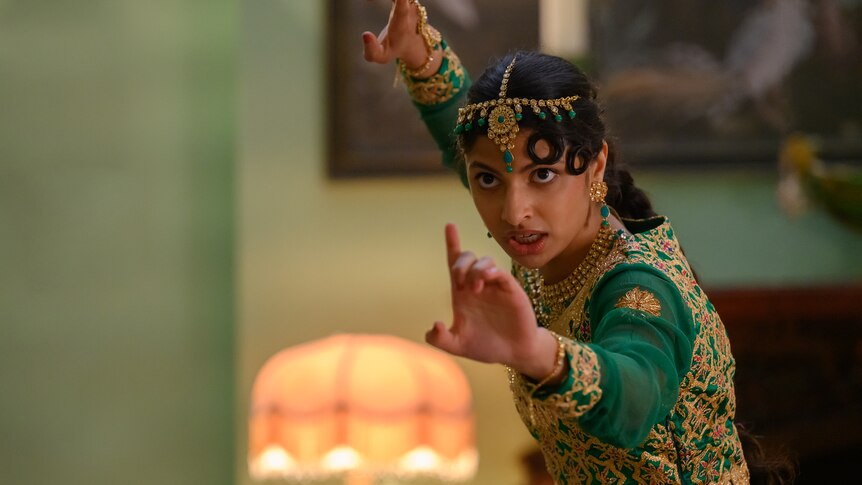 Priya Kansara, a young Pakistani woman with dark hair wearing a vibrant green sari and gold head jewellery strikes a combat pose