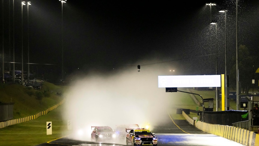 Water sprays from the race track at night with super cars sliding in the wet