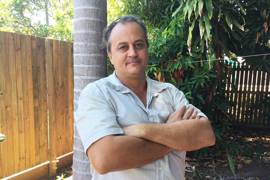 Townsville jobseeker Chris McCoomb stands in his backyard with his arms crossed.