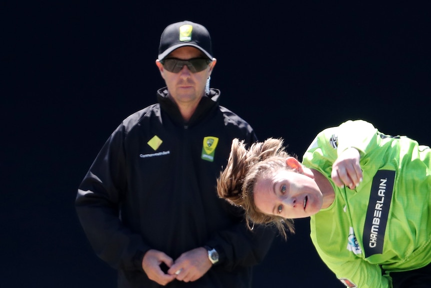 Sam Bates leans forward after bowling a cricket ball.