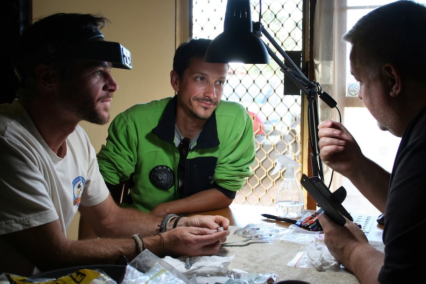 Three men sitting at a table inspecting a piece of opal.