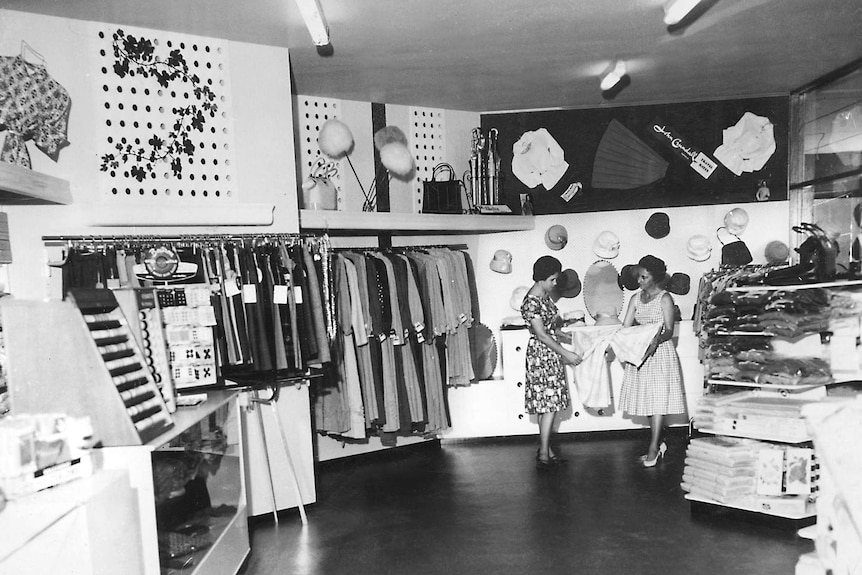 A black and white photo showing a clothing store, with two women looking at clothing, taken in 1963.