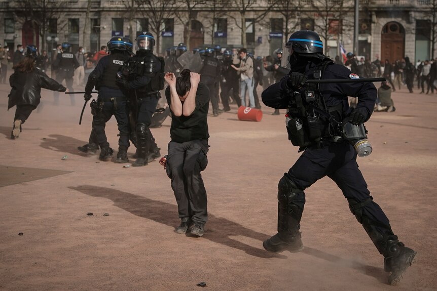 a police officer in riot gear prepares to hit a demonstrator with a baton as police and demonstrators scuffle in Lyon