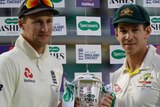 Joe Root and Tim Paine smile awkwardly while holding a large silver trophy.