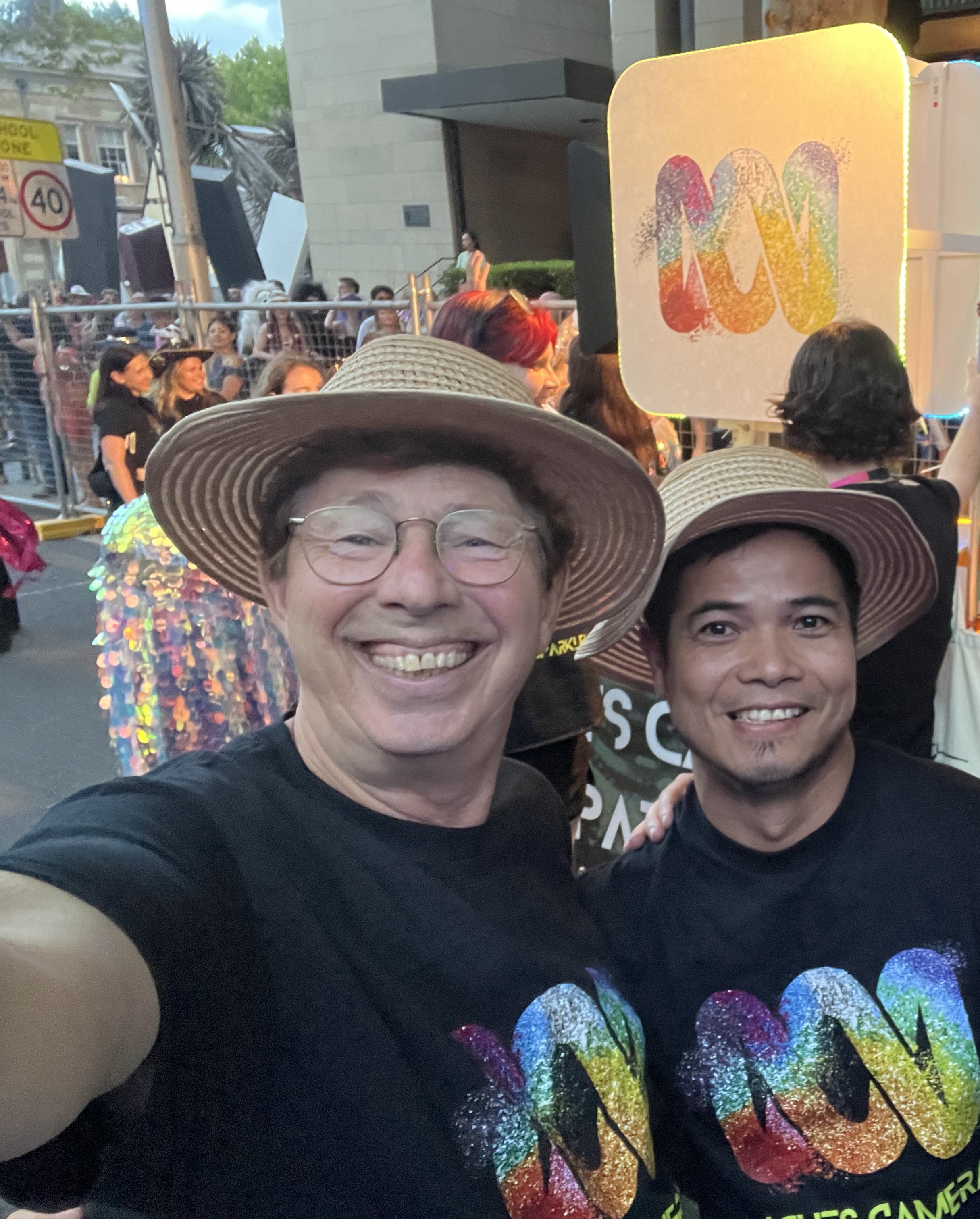 Jerry and Tuan grinning at a parade, surrounded by confetti, wearing ABC shirts in rainbow