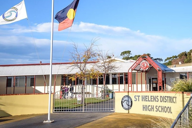 white school building with a yellow fence, Aboriginal and Australian flags flying, sign saying St Helens District high school 