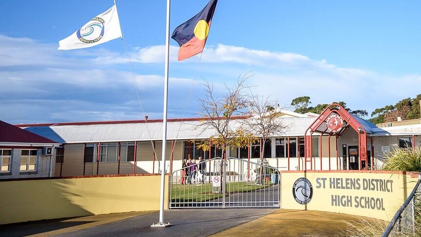 white school building with a yellow fence, Aboriginal and Australian flags flying, sign saying St Helens District high school 