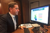 Queensland State Development Minister Cameron Dick sits in front of a computer.