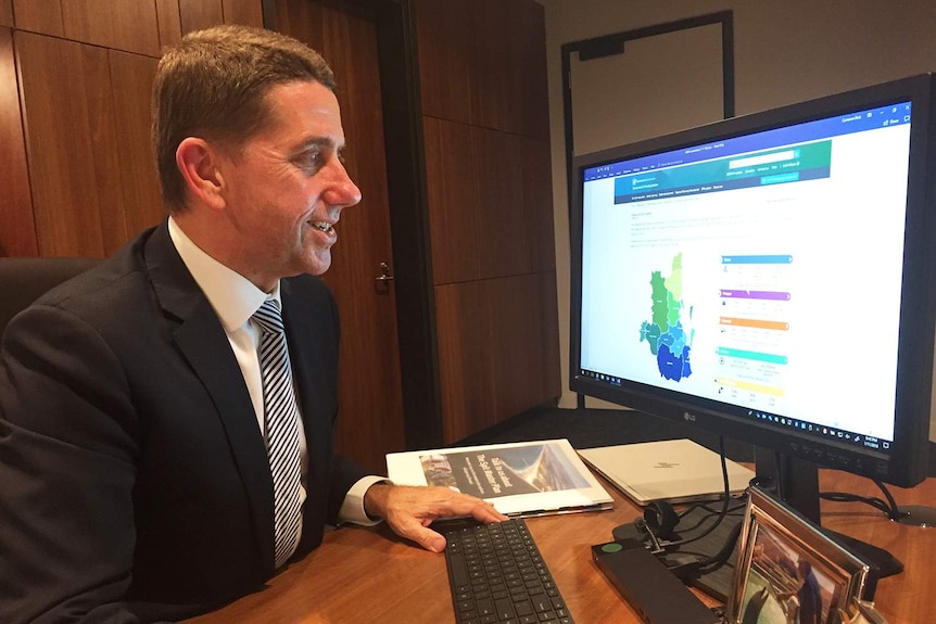 Queensland State Development Minister Cameron Dick sits in front of a computer.