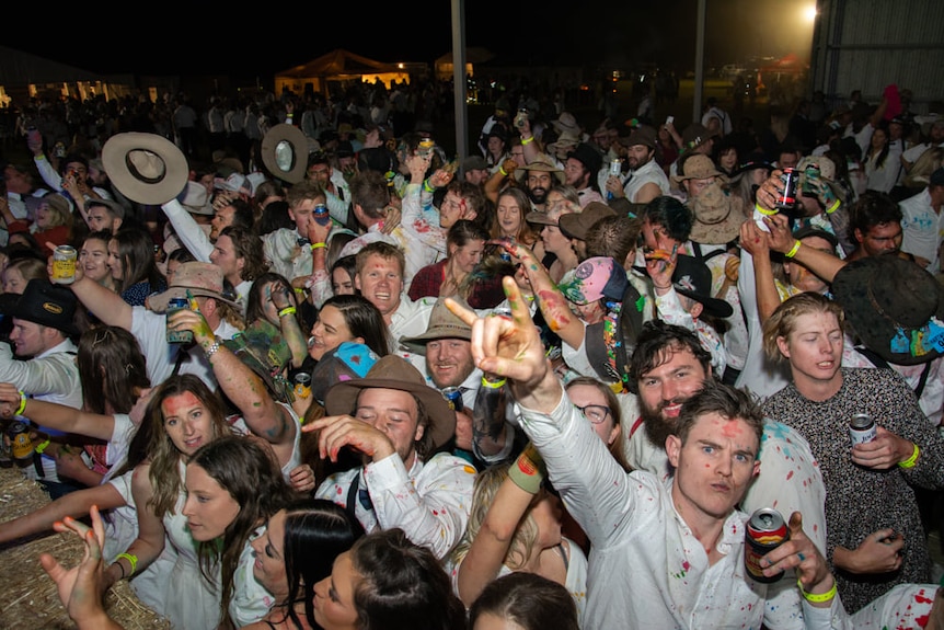 A crowd covered in food dye and carrying Akubra hats smiles and makes gestures to the camera