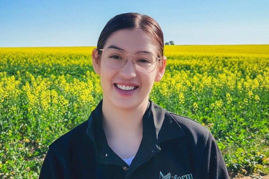 A woman in a black polo shirt stands in front of a canola fieldd