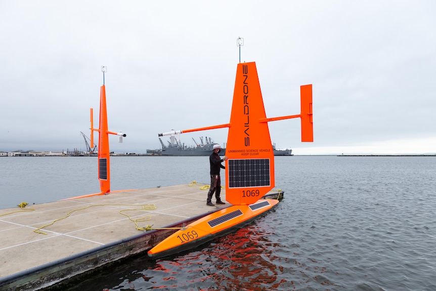 Two bright orange sail drones alongside a wharf