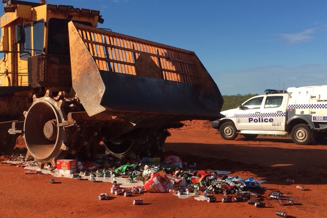 A giant bulldozer crushes cans of beer and spirits on red dirt.