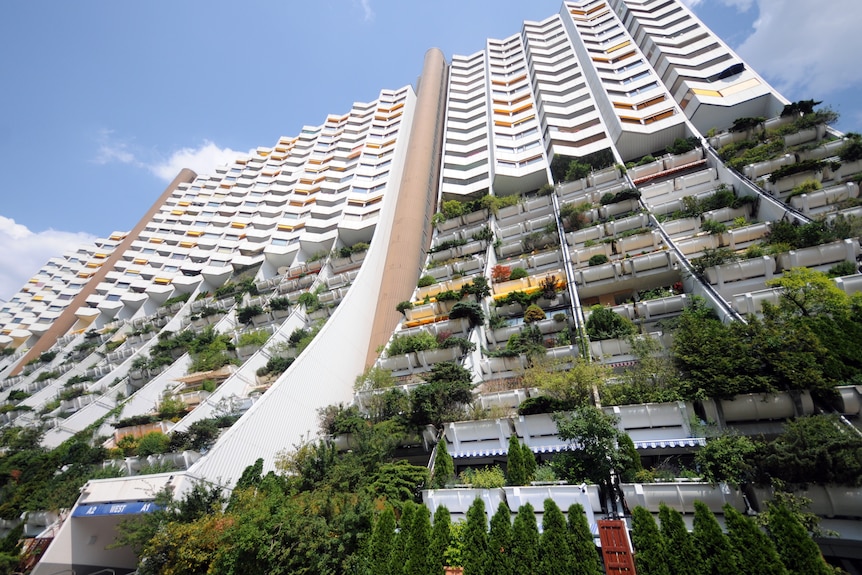 A huge 1970s apartment building, with white balconies, many of which feature lush gardens