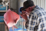 A man air-brushing a mould of a fish pink. 