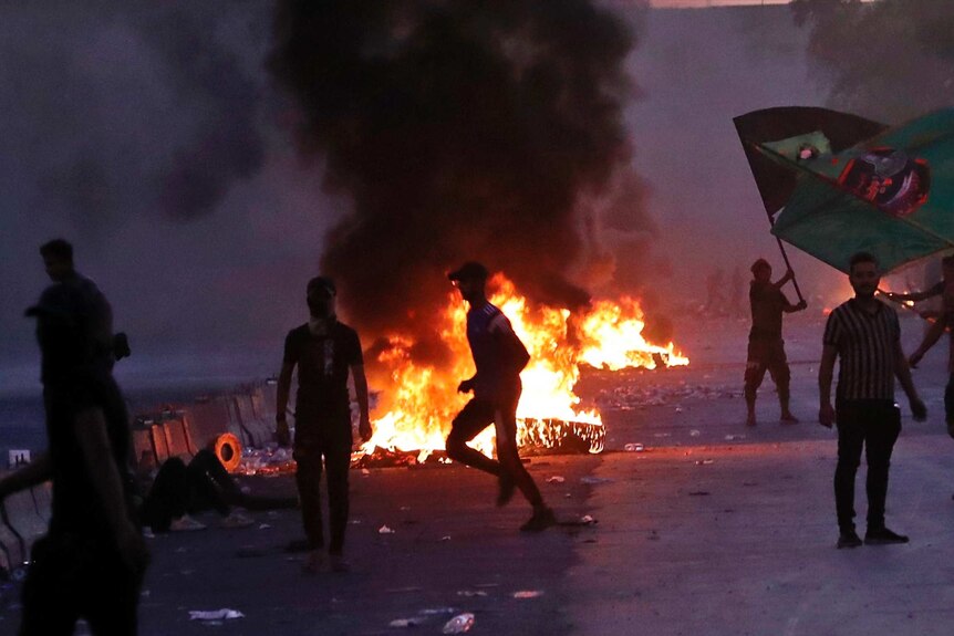 Anti-government protesters set fires as they rally on a closed Baghdad street. Smoke fills the air.
